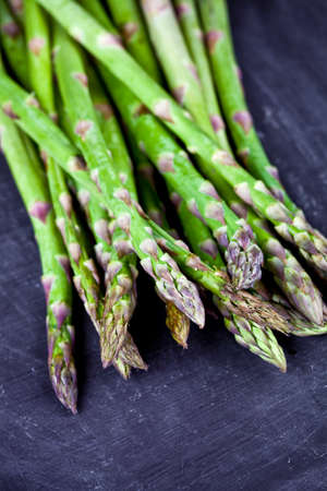 Organic fresh raw garden asparagus closeup on black board background. Green spring vegetables. Edible sprouts of asparagus. With copy space.の写真素材