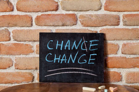 Black board with the phrase CHANCE CHANGE drown by hand on wooden table on brick wall background. For business presentation.の写真素材