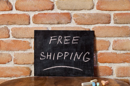 Black chalkboard with the phrase FREE SHIPPING drown by hand on wooden table on brick wall background. For business presentation.の写真素材