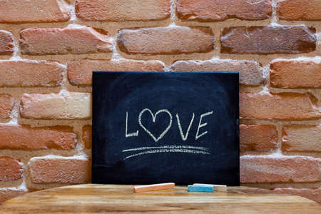 Black board with the word "Love" drown by hand on wooden table on brick wall background. Love concept.の写真素材