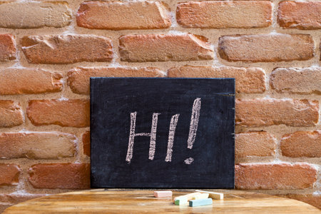 Black board with the word HI! drown by hand on wooden table on old brick wall background.の写真素材