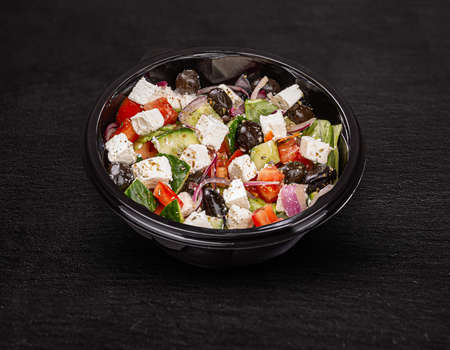 Tasty greek salad with feta, olives and tomatoes in a plastic bowlの写真素材