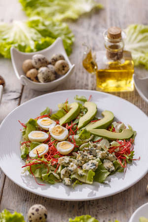 Salad with avocado, quail egg and blue cheese in a white plateの写真素材