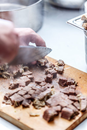 The cook cuts boiled beef meat on wooden cutting boardの写真素材