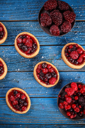 Tartlets with fresh red berries on blue wooden background
