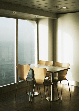 Empty table and chairs by a window on a ferry at seaの素材