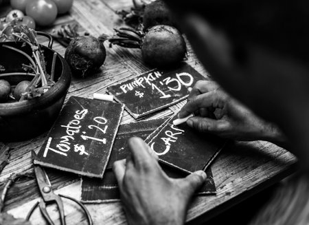 Rear view of man writing vegetable price on chalk board grayscaleの素材
