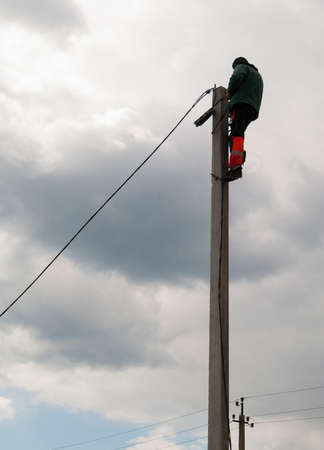 electrician climbed to the top of a concrete pillar and fixes it on cableの写真素材