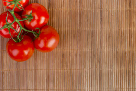 branch of ripe tomatoes on a bamboo table clothの写真素材