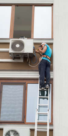 man standing on a ladder and sets the air conditioner outdoor unitの写真素材