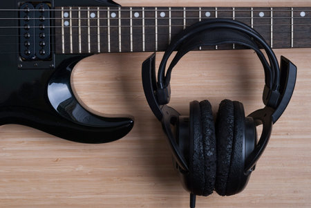 black electric guitar and headphones on a wooden background texture