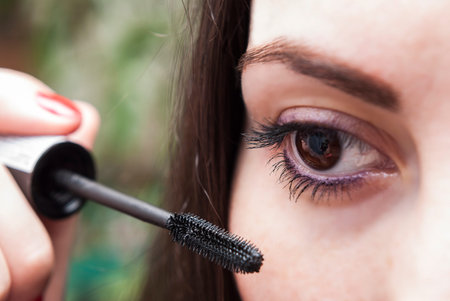 young woman paints the lashes mascara while looking in the mirror