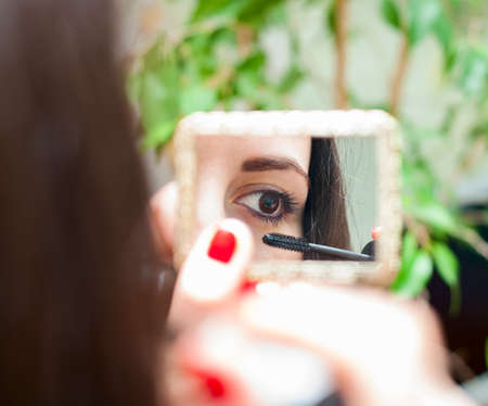 young woman paints the lashes mascara while looking in the mirrorの写真素材