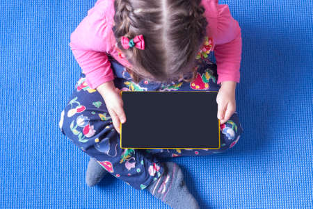 girl looking at tablet sitting on a blue matの写真素材