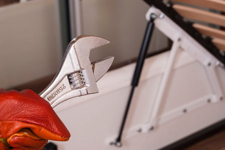 worker holds a wrench against the background of the lifting mechanism of the bed