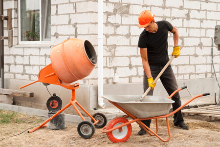 construction worker with a shovel in his hands loads a concrete mixer