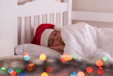 cute little girl in santa hat lies on the bedの写真素材