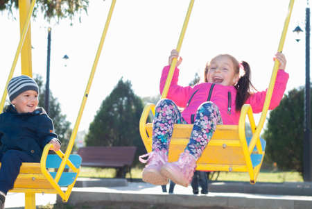 little girl and boy ride on a swingの写真素材