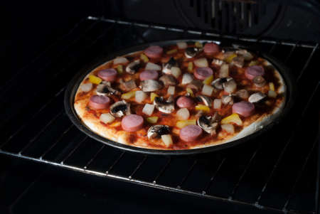 pizza with sausage and mushrooms in an electric ovenの写真素材