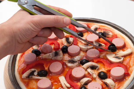 cook is laying out the ingredients for the pizza on the dough sheetの写真素材