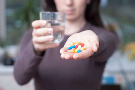 woman holding a glass with water and giving pillsの写真素材