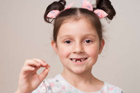 Charming little girl smiling and holding a milk toothの写真素材
