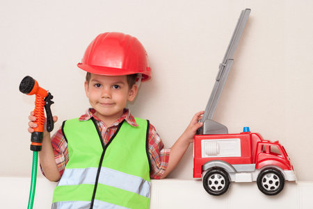 little boy in a red helmet and with a hose in his hands imagines himself to be a fireman