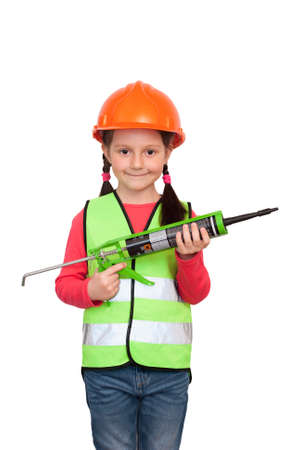 little girl in uniform and helmet holds a pistol with a bitumen sealant and imagines herself an industrial workerの写真素材