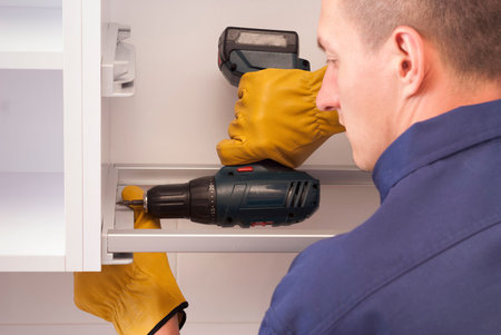 worker with screwdriver assembles and installs furniture in the kitchen