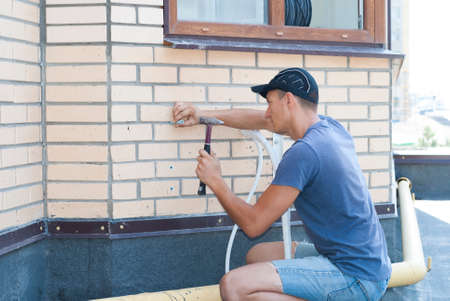 the worker installs the outdoor unit of the air conditioner on the wall of the houseの写真素材