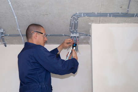 electrician strips wires in junction box on ceilingの写真素材