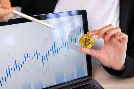 Business woman hold bitcoin actual coin in hand, background with computer laptop