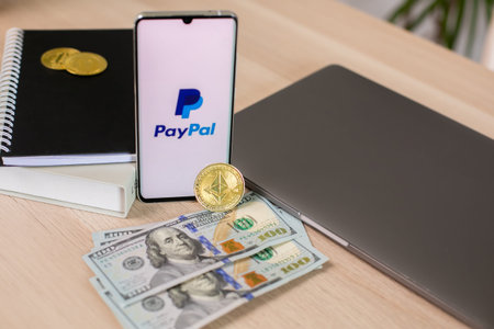 Lodz, Poland - June 21, 2022: Paypal application on smartphone near dollar bills and crypto currency...