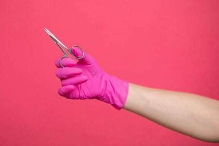 A hand in a protective glove holds manicure scissors.