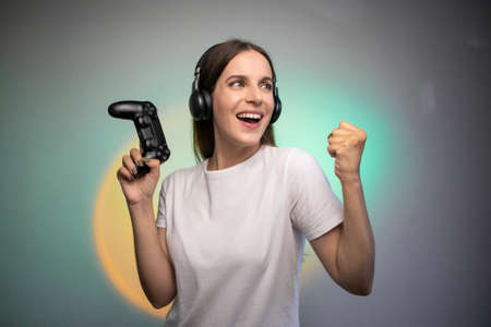 Game win. Happy female gamer in headphones rejoices in the victory in the game. Emotional gamer. Portable game consoleの写真素材