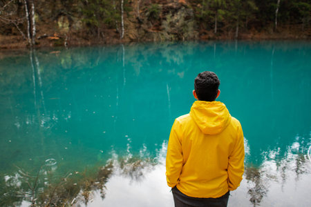 Man in a yellow jacket near a blue mountain lake. Tourism inspiration