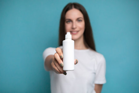 Young woman with bottle of solution for lenses on blue background. Mock up of liquid for lenses
