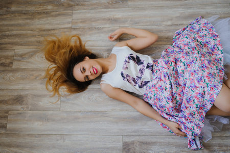 happy young woman lying on wooden parquet floor relaxed at home looking upの写真素材