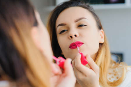 portrait in mirror of sexy smiling caucasian young woman model with glamour red lips, bright makeup, eye arrow makeup, Perfect clean skin. white teeth, applying lipstick の写真素材