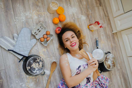 young woman lying on the floor in a vintage kitchen very sad. orange, eggs, apples, flour around herの写真素材