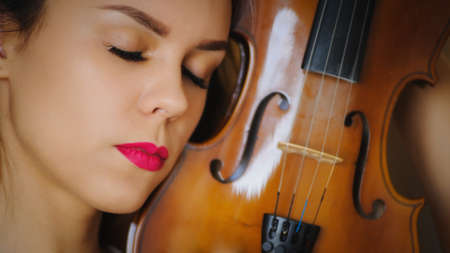 Music portrait of young woman. Violin play. Close up face beautiful modelの写真素材