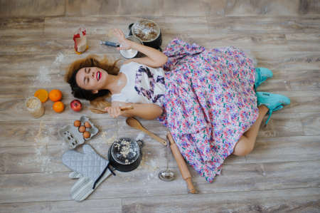 young woman lying on the floor in a vintage kitchen very sad. orange, eggs, apples, flour around herの写真素材