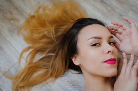 happy young woman lying on wooden parquet floor relaxed at home looking upの写真素材
