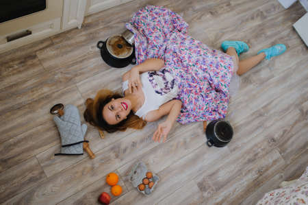young woman lying on the floor in a vintage kitchen very sad. orange, eggs, apples, flour around herの写真素材
