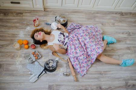 young woman lying on the floor in a vintage kitchen very sad. orange, eggs, apples, flour around herの写真素材