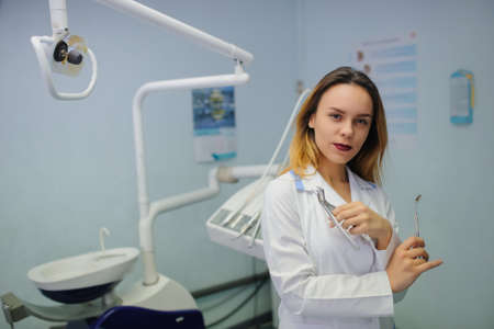 portrait of smile young woman dentist in dental treatment room with mirror and forcepsの写真素材