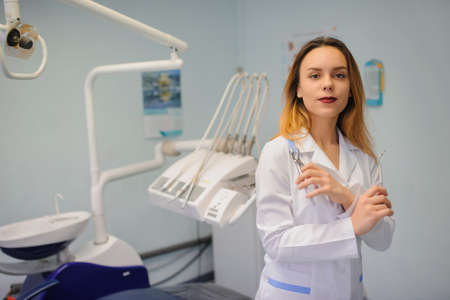 portrait of smile young woman dentist in dental treatment room with mirror and forcepsの写真素材