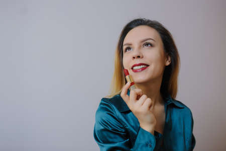 Portrait of sexy smiling happy caucasian young woman applying red lipstick on lips and looking at herself in the mirrorの写真素材