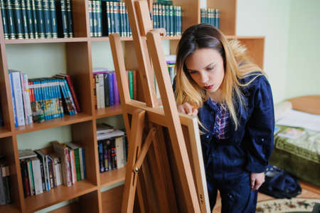 Attractive young woman artist begins to draw a new paint on a  wooden easel, holds brush.の写真素材