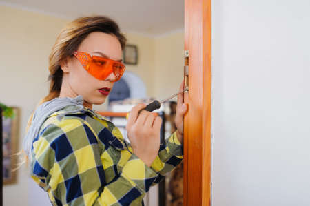 A young woman builder working using a screwdriver and fix the door. Orange protective glassesの写真素材